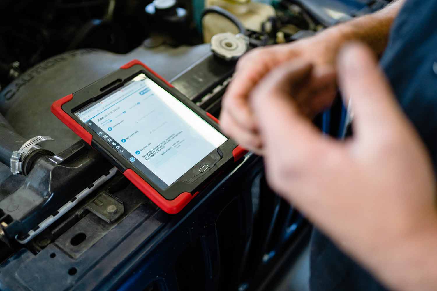 person looking at a software tool on an ipad that's under the hood of a car