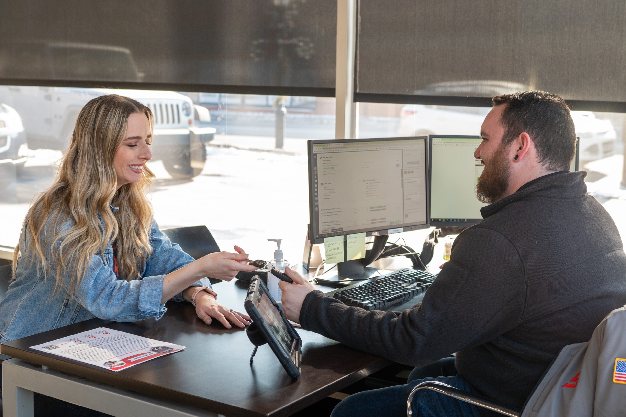 Service Writer handling keys to happy customer in front of computer